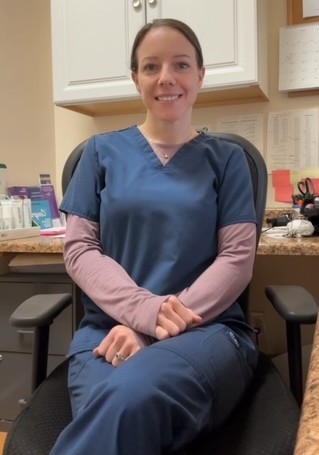 Chiropractic Elkton MD Emily Sparco Meet The Team Emily Sparco, receptionist, sitting at desk in blue scrubs with legs crossed.